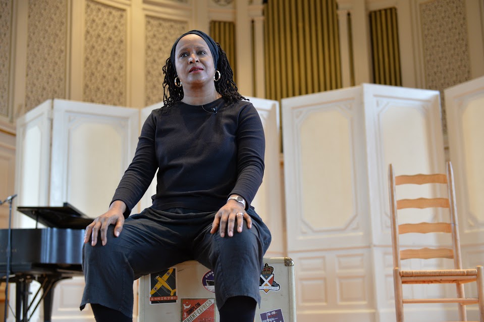 Dr. Mary E Weems, dressed in all black, sitting on a chair, addressing the audience