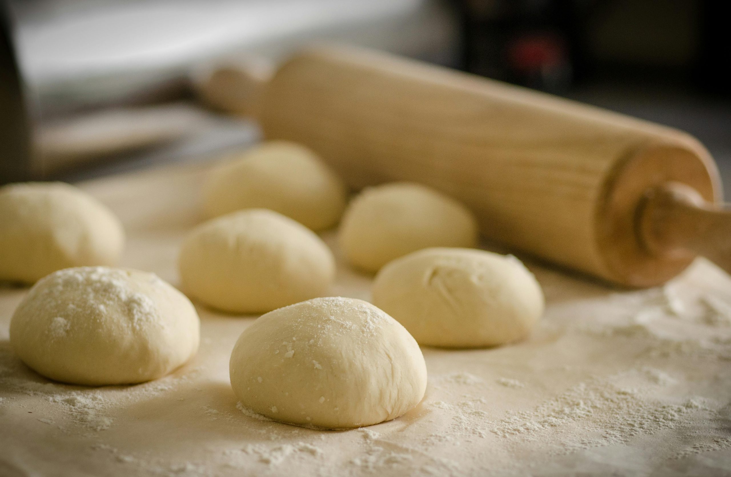 six balls of dough covered in flour with rolling pin 